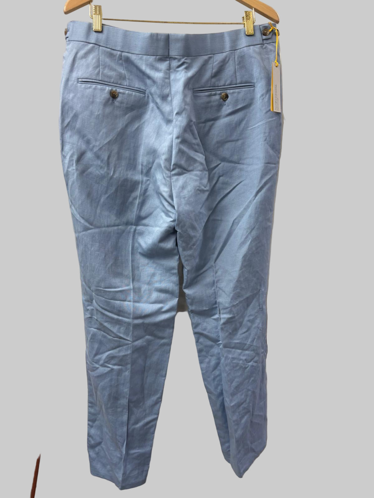 Light blue pants hanging on a wooden hanger against a white curtain.